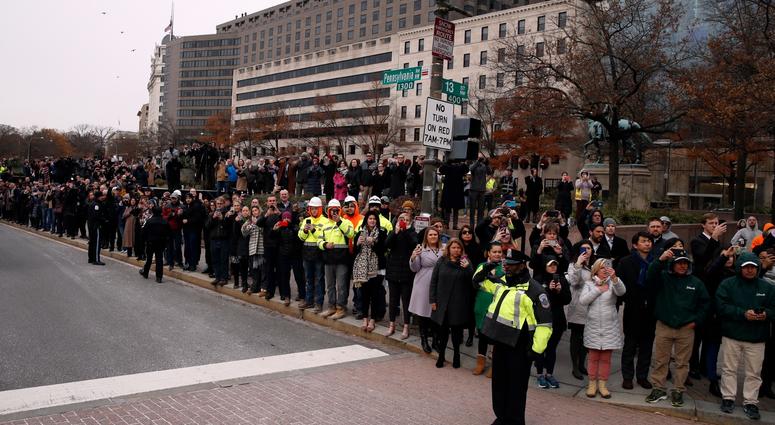 People watch as the hearse carrying the flag-draped casket of former President George H.W. Bush passes Freedom Plaza on its way to a State Funeral at the National Cathedral December 5, 2018 in Washington, DC. George H.W. Bush