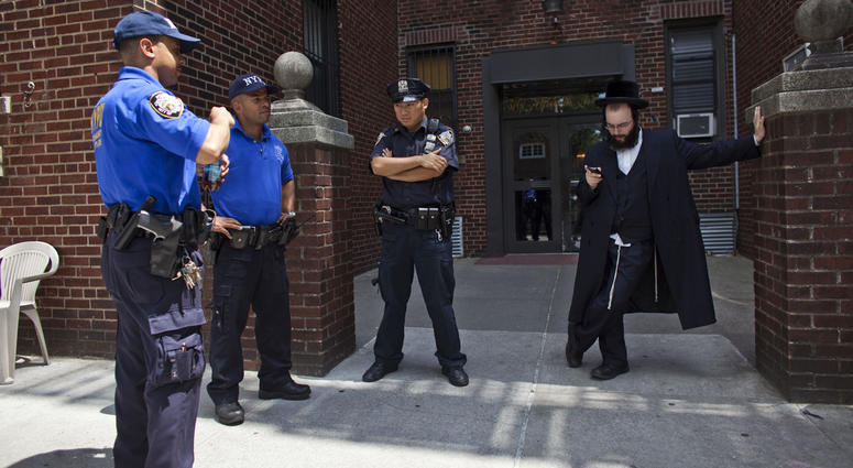 A Hasidic man checks his phone as members of the New York Police Department stand guard in front of the residence in Borough Park on July 13, 2011. Hasidic man protected by NYPD