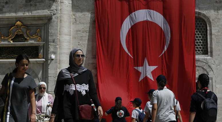 People walk past a Turkish flag on a mosque compound in Istanbul, Wednesday, Aug. 15, 2018. Istanbul, Turkey