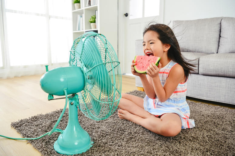 child eating watermelon with two hands. sitting in front of the electric fan child eating watermelon with two hands. sitting in front of the electric fan