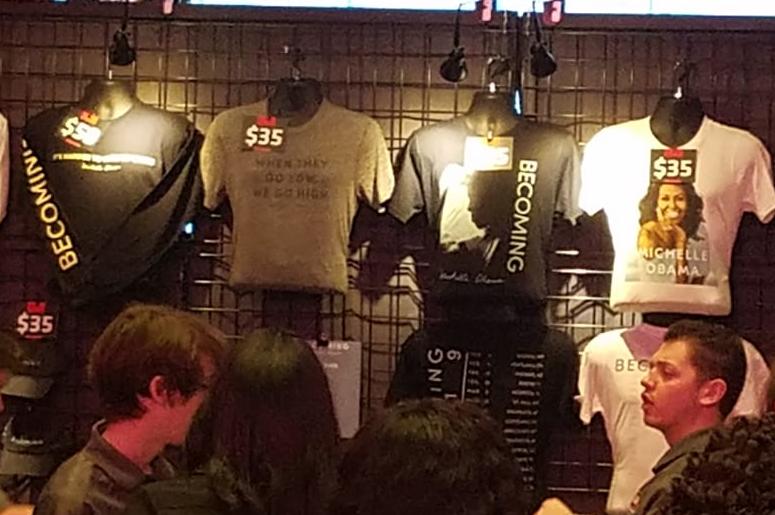 Similar to a concert, event-goers stood in line to purchase merchandise showcasing the "Becoming" tour event. Similar to a concert, event-goers stood in line to purchase merchandise showcasing the "Becoming" tour event.