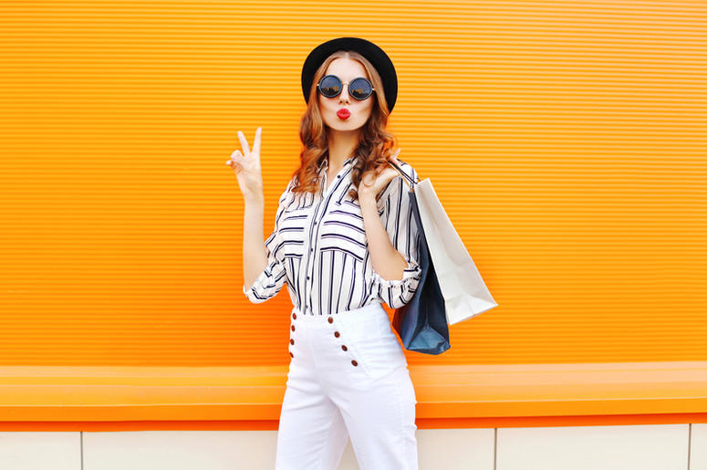 Fashion young girl with shopping bags wearing a black hat white pants over colorful orange Fashion young girl with shopping bags wearing a black hat white pants over colorful orange